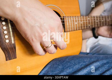 Close up of man hand playing acoustic guitar indoors during home music practice. Creative hobby, acoustic music and leisure lifestyle concept with str Stock Photo