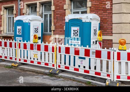 Two Toi Toi portable toilets behind red and white safety barriers at a street construction site in Germany. Stock Photo