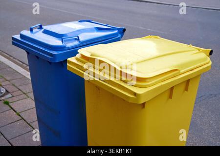 A blue and a yellow plastic recycling bin standing side by side on a city street pavement for waste collection. Stock Photo