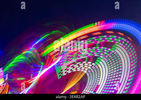 Merry-go-round carousel at night with many colorful LED light circles. Long time exposure that leaves abstract circular moving light traces and painti Stock Photo