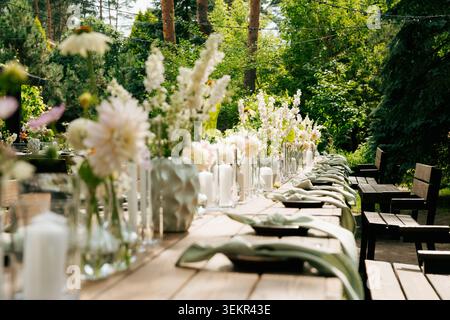 Outdoor garden wedding reception table with floral centerpieces, pillar candles, sage napkins and fairy lights set in a lush green forest backdrop Stock Photo