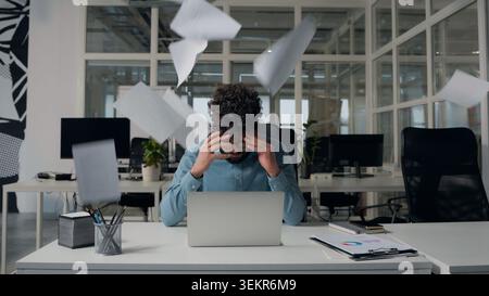 Irritated stressed Arabian business man working with papers throwing documents away holding head laptop work problem failure ethnic businessman male Stock Photo
