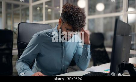 Stressed suffering Arabian business man holding head suffer thinking headache problem deep in thoughts with problem work typing computer at office Stock Photo