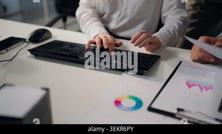 Close up female hands typing computer keyboard male with papers diagram stats Caucasian smiling business woman using pc with unrecognizable men Stock Photo