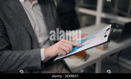 Close up male hands holding tablet folder paper reviewing charts unrecognizable business man reading graphs statistical data sales results businessman Stock Photo