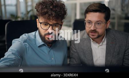 Two concentrated multiracial businessmen looking in computer screen monitor talking diversity business men working talk Arabian and Caucasian males Stock Photo