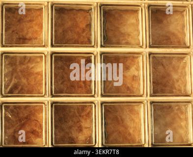 A full-frame texture of a square glass block wall illuminated from behind with a cozy, warm amber light showing subtle wavy patterns. Stock Photo