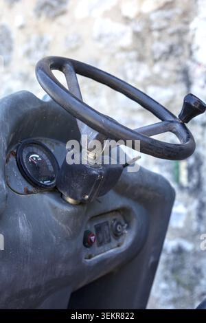 Close-up view of a worn steering wheel with a spinner knob and the dusty control dashboard panel of heavy industrial machinery or a roller. Stock Photo