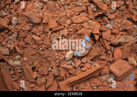 Full frame background filled with crushed terracotta clay roof tiles, brick fragments, and debris, featuring a unique blue accent piece in the center. Stock Photo