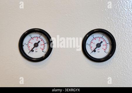 Two circular analog pressure gauges with black bezels installed side by side on a clean white surface. Stock Photo