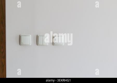Three white light switches on a light wall Stock Photo