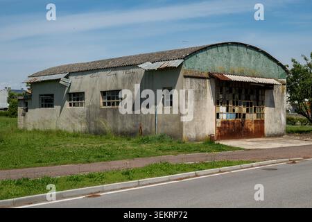 This weathered, abandoned warehouse sits by a quiet road. Its broken windows and rusted metal doors highlight the decay and passage of time in this fo Stock Photo