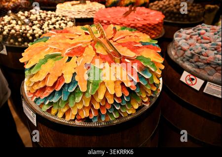 Stacked multicolored gummy crocodile candies with metal tongs in a bulk candy display — close-up for sweets, retail, confectionery and food themes. Stock Photo