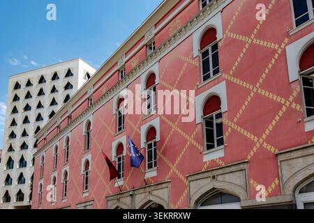 The pink painted facade of the Ministry of Infrastructure and Energy features yellow lattice patterns and flags in Tirana, Albania. Stock Photo