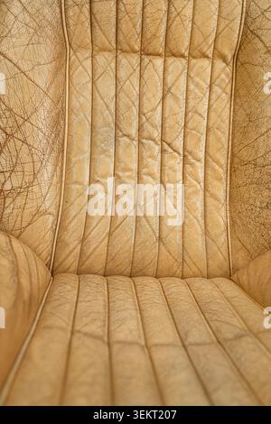Direct full-frame view displays the vertical ribbed design and intricate cracked texture of worn tan leather upholstery, highlighting natural aging pa Stock Photo