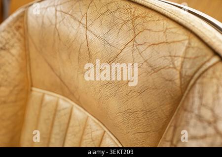 Extreme close-up view highlights the fine details of surface cracking, creases, and worn texture lines on a light brown premium leather car seat backr Stock Photo