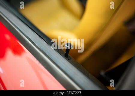 Detailed interior shot focuses on a black manual door lock pin protruding from the window sill, with the soft-focus, vibrant yellow leather upholstery Stock Photo