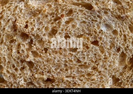 Granary bread in close-up, revealing a rustic texture with airy holes, wholegrain flecks and a freshly baked golden-brown interior Stock Photo