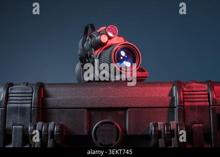Professional lightweight night vision monocular with gen 3 tube and waterproof housing standing on black plastic protective case under red studio ligh Stock Photo
