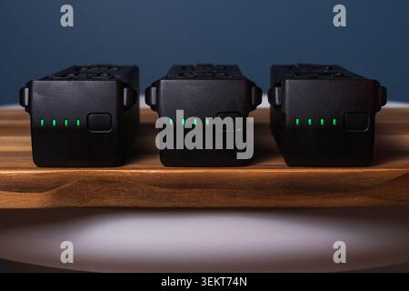 Three drone smart batteries with fully charged green led indicators placed in a row on a wooden shelf surface close-up Stock Photo
