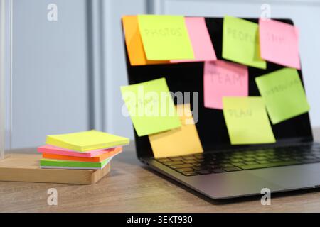 Computer with colorful sticky notes on wooden table, selective focus. Multitasking, deadline and rush at work Stock Photo