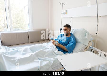Male patient using smartphone recovering in hospital bed Stock Photo