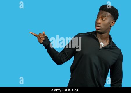 Young black man pointing to the side with a surprised look on a blue background Stock Photo