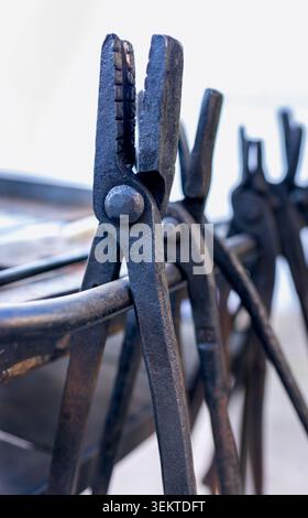 Traditional blacksmith tools with a heavy steel anvil, hammer, and vintage metal tongs on a rustic wooden workbench. Professional forging equipment. M Stock Photo