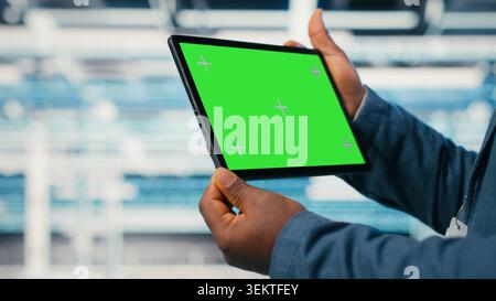 Green screen tablet used by data center worker to manage enterprise cloud computing IT solutions using laptop. Admin using mockup touchscreen device to monitor futuristic server farm, camera B Stock Photo