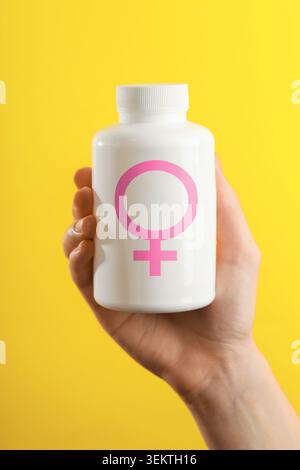 Female hormones. Woman holding pill bottle with female gender symbol on yellow background, closeup Stock Photo