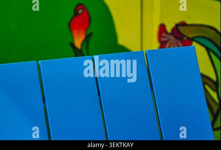 A bright blue Adirondack bench in front of a colorful mural Stock Photo