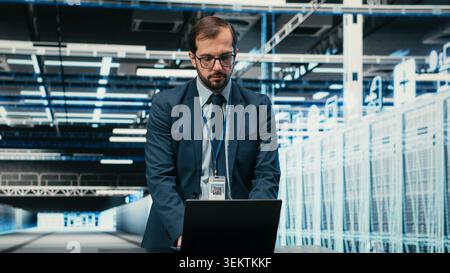 Data center technician using laptop and augmented reality to install upgraded server racks systems. Worker using automation tools to monitor server farm performance, VFX overlay, camera B Stock Photo