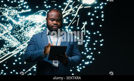 Computer scientist optimizes neural network neurons map with tablet and AR simulation tech. African american man fine tuning machine learning AI model synaptic weights with device, camera B Stock Photo