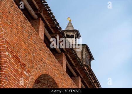 Brick Fortress Tower Under Pale Sky, Red Brick Wall With Round Arches, Wooden Spire Crowned With Gilded Cross, Weathered Masonry Textures, Stock Photo