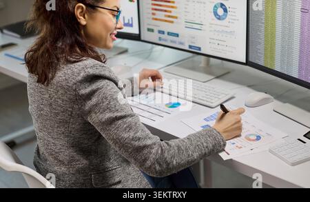 Female accountant analyzing financial data on computer monitors with spreadsheets Stock Photo