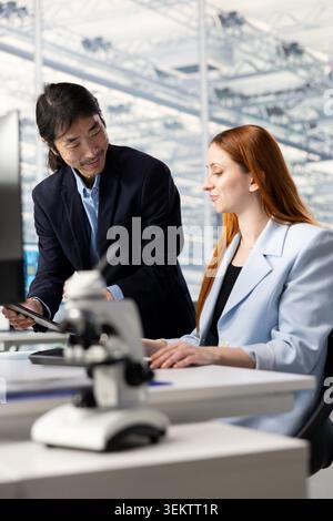 Observing microchip layout, microscope equipment and woman with senior manager in RD office. Doing innovative study, microscopy tool and Asian man with coworker researching materials Stock Photo