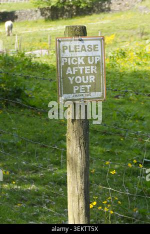 Wooden post with a public warning sign reading please pick up after your pet on a green grassy trail bank on a bright day in Bolton, UK Stock Photo