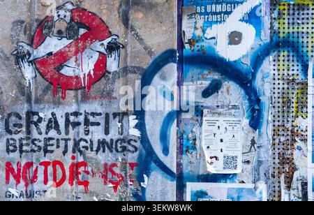 Graffiti reading "Graffiti Beseitigungs Notdienst" (graffiti removal emergency service) on a wall covered with street art, tags and posters. Stock Photo