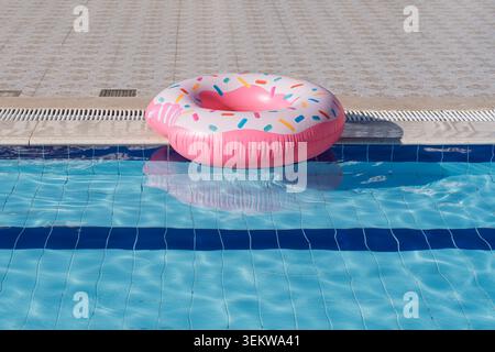 Pink donut pool float floating in a swimming pool on a sunny day, summer vacation concept Stock Photo