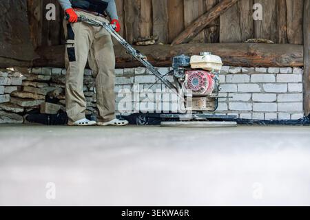 Concrete finishing worker using power trowel tool to smooth surface of new floor slab Stock Photo