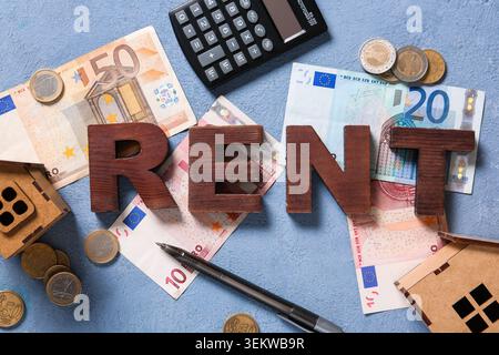 Word RENT with money, calculator and wooden houses on blue grunge background Stock Photo