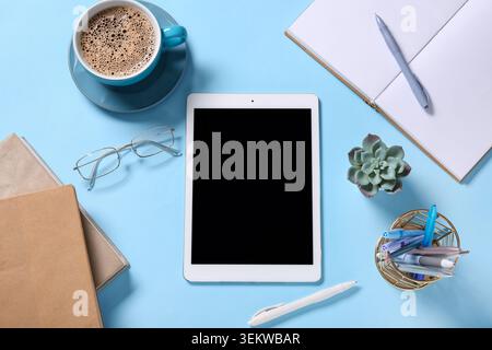 Tablet computer with cup of coffee, eyeglasses and stationery on blue background Stock Photo