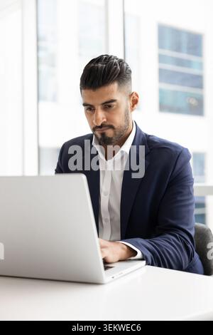 Focused Indian businessman working on laptop at office table Stock Photo