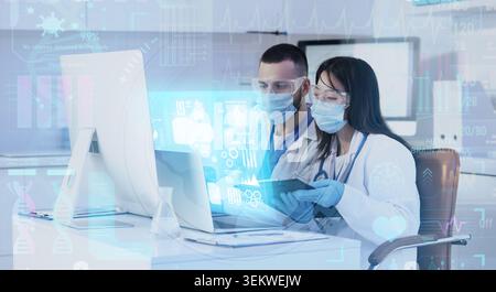 Doctors analyzing medical data on computer in hospital office with digital healthcare interface, protective masks, goggles, tablet and stethoscope, te Stock Photo