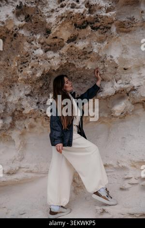 Woman rock nature explores textured sandstone formations in a stylish outfit while touching the rugged cliff surface Stock Photo