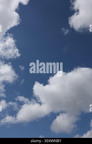 Dramatic White Clouds Against Deep Blue Summer Sky. Close-up view of fluffy white clouds floating across a vivid blue sky. Stock Photo