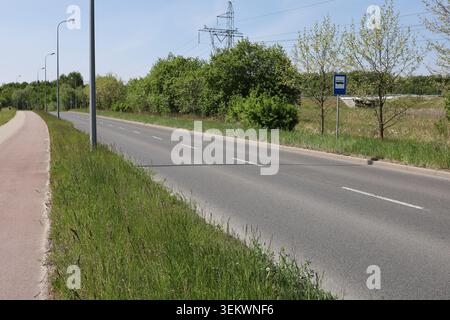 Asphalt road running through a green rural landscape with trees, grass, and utility infrastructure visible in the distance. Stock Photo