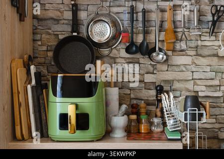 Kitchen counter with air fryer and various cooking tools like pans and utensils. Bright light shines on the wooden surface showing a tidy kitchen spac Stock Photo