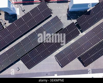 Solar panels are installed on a flat rooftop in an urban area. The panels collect sunlight to generate electricity. The setup shows rows of dark panel Stock Photo