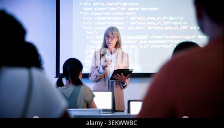 Professor, students and presentation with tablet in classroom, programming course and IT curriculum. University, people or mature lecturer with Stock Photo